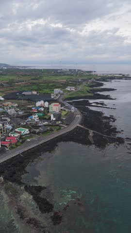 Coastal Houses And Road Along Dark Volcanic Rocky Shoreline Near Haengwon Beach In Gujwa-eup, Jeju Island, South Korea. - aerial vertical shot