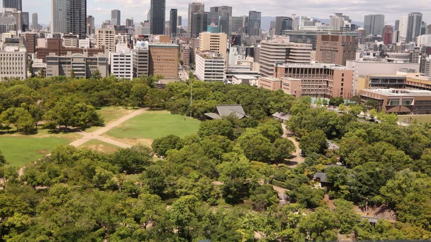 aerial view across the green landscape of Osaka Castle Park toward the modern urban skyline of Osaka, Japan, combining historic surroundings with contemporary city architecture