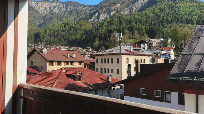 A woman enjoying a moment drinking coffee on a balcony with a panoramic view of Lozzo Di Cadore village and the majestic Dolomites mountains in Italy. Captures authentic travel and lifestyle.-
