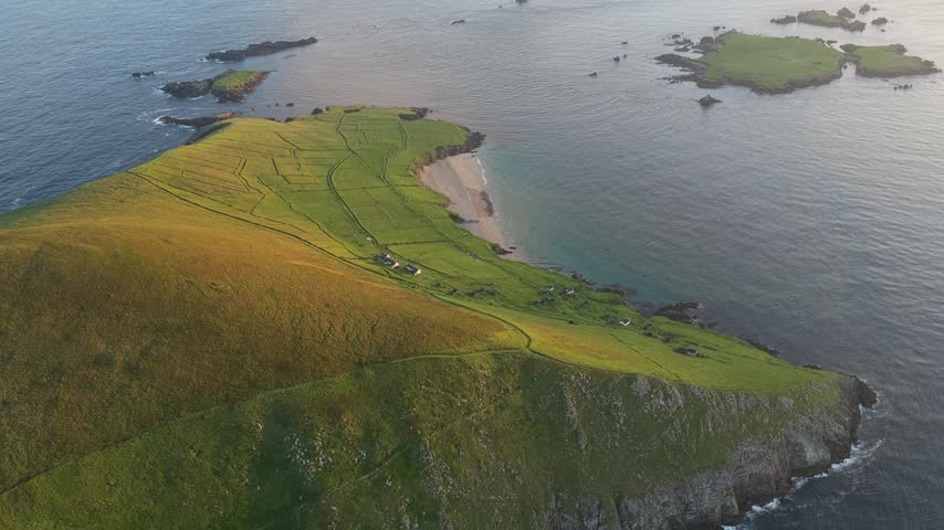 Drone shot over patchwork green fields and an ocean-facing headland on Great Blasket Island, County Kerry.