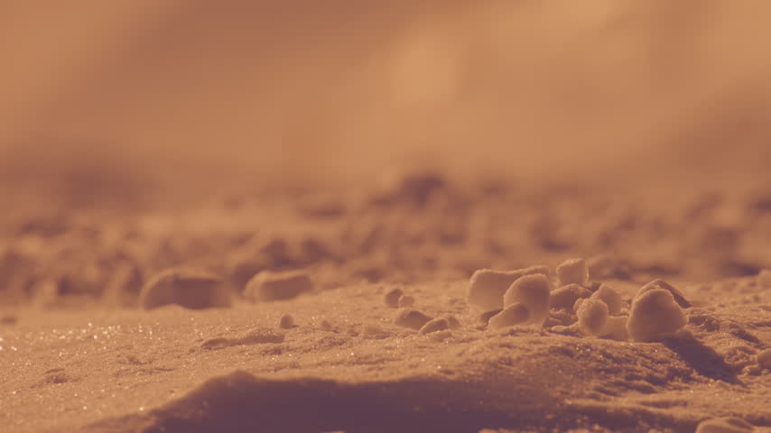 Shallow-focus close-up reveals small clumps and crystals across sunlit alpine snow