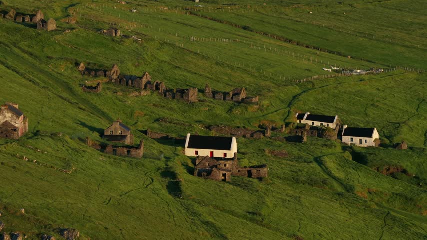 Drone view of traditional stone cottages scattered across the green hillside of Great Blasket Island on Ireland