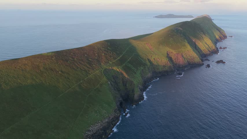 Wide aerial view along the rugged green headland, steep coastal cliffs and Atlantic shoreline of Great Blasket Island.