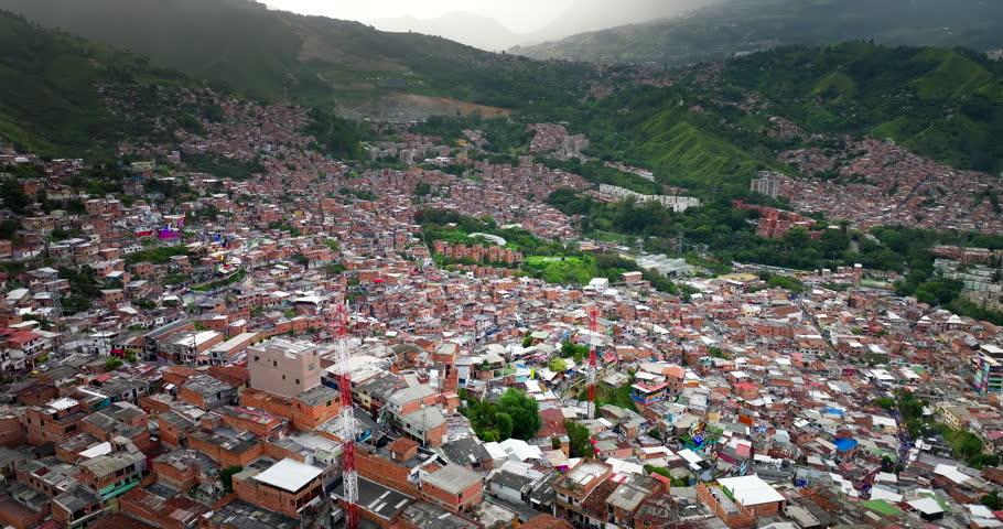 Densely populated Comuna 13 neighborhood with brick houses sprawling across the green hillside in Medellin, Colombia. Aerial drone orbiting