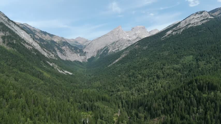 Rocky mountain ridge rises alongside dense forest in Fernie, British Columbia, Canada, within the forested landscape of the Elk Valley and Rocky Mountains - drone shot