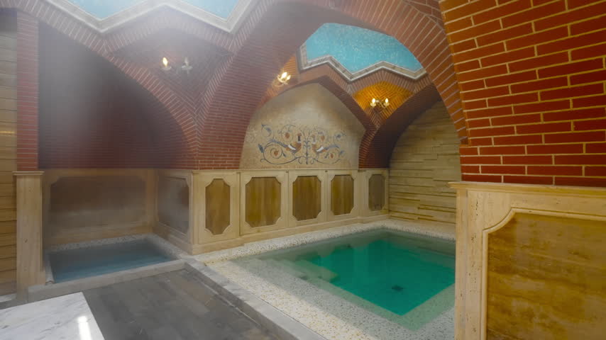 A private sulphur bath room in Tbilisi with a turquoise pool, brick vaults and painted panels lit by warm wall lamps.