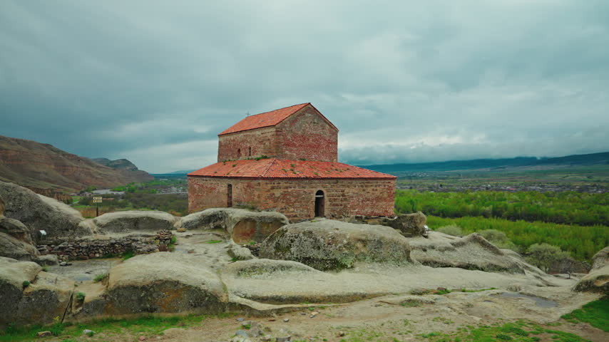 Heavy grey clouds gather above the red roofed brick basilica standing on the rock terraces of Uplistsikhe.