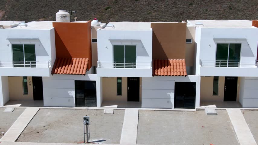 Aerial view showing modern white townhouses with terracotta roof awnings and balconies arranged along a paved residential area in Mexico.