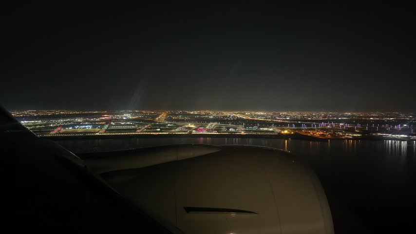 Slow motion view from an airplane passenger window overlooking the jet engine during night approach and touchdown on the illuminated runway at Hamad International Airport in Doha, Qatar.