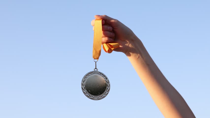 Woman with silver medal outdoors, low angle view. Slow motion effect