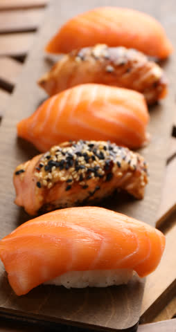 Taking nigiri sushi with chopsticks from wooden table, closeup