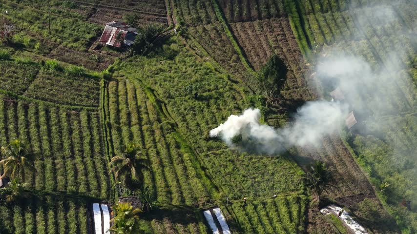 Agricultural Crop Fields And A Rural Wooden Hut With Smoke Rising In Bukit Dewangga, Sidemen, Indonesia. - aerial shot