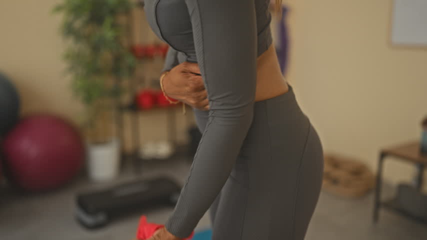 Woman holding red resistance band and gripping abdomen during yoga training in a studio; strength focus.
