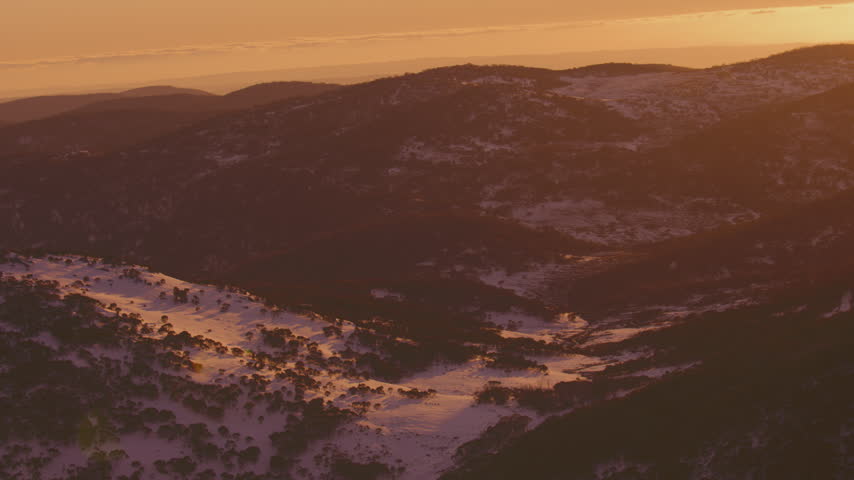Snowy alpine valley and layered mountain ridges glow in warm light near sunset