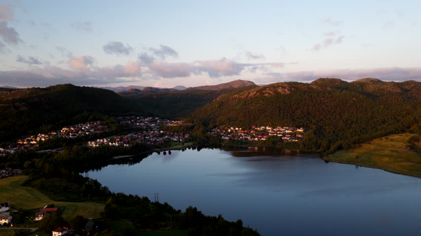 Peaceful village nestled in valley next to calm lake at sunset in Hommersak, Norway. Aerial forward