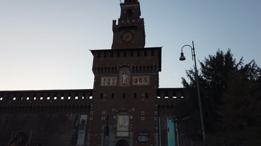 Iconic Torre del Filarete of Castello Sforzesco towering over the tree canopy of Parco Sempione in Milan. Classic Italian historical architecture framed by urban nature.