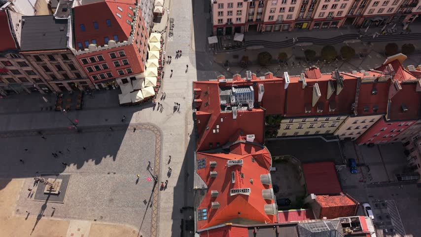 Aerial view of vibrant urban square in Wroclaw, Poland, showcasing red-roofed buildings, outdoor cafes, and pedestrians enjoying a sunny day