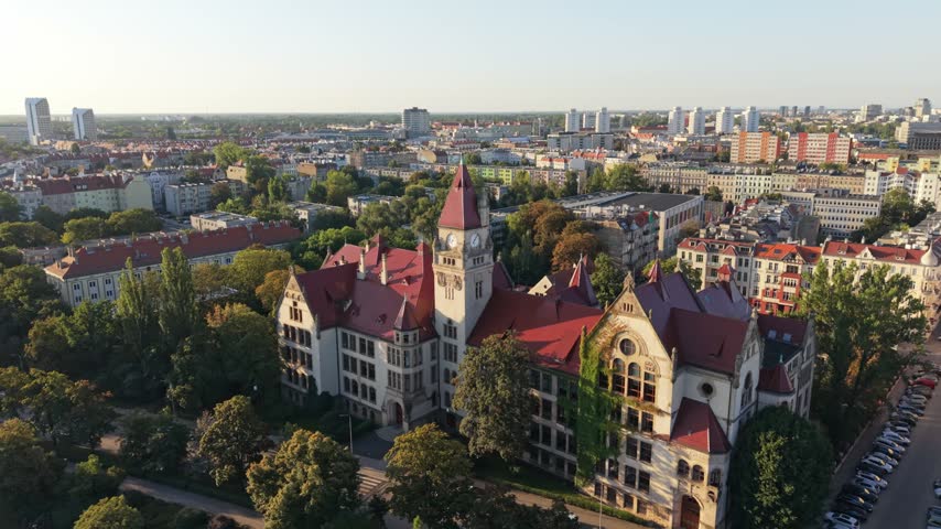 Aerial view of historic architecture in Wroclaw, Poland, showcasing a beautiful park, trees, and city skyline under clear blue skies during golden hour