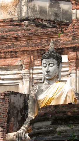 Stone Buddha statue draped in yellow cloth rests before ancient brick ruins in Ayutthaya.