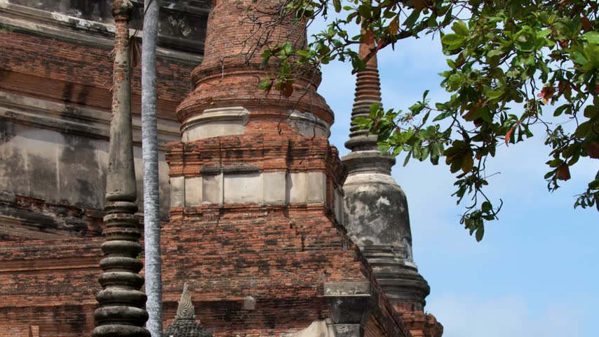 Camera tilts down from ancient brick stupas to reveal a draped Buddha statue in Ayutthaya.