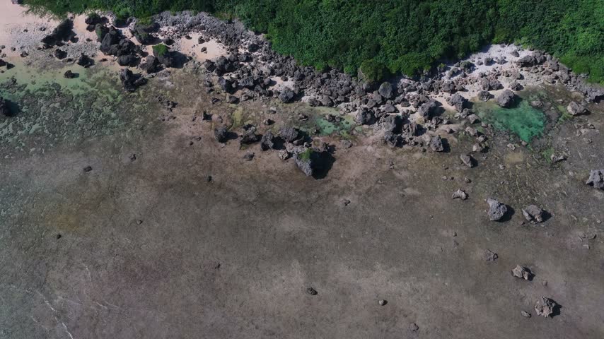 Aerial view of shallow coastal water with scattered rocks, a sandy beach, and dense green vegetation along Boraga Beach in Miyako, Okinawa, Japan