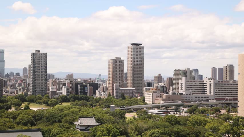 Wide cityscape view featuring the historic Osaka Castle standing amidst the modern urban skyline of Osaka, Japan. Japanese cultural landmark and park