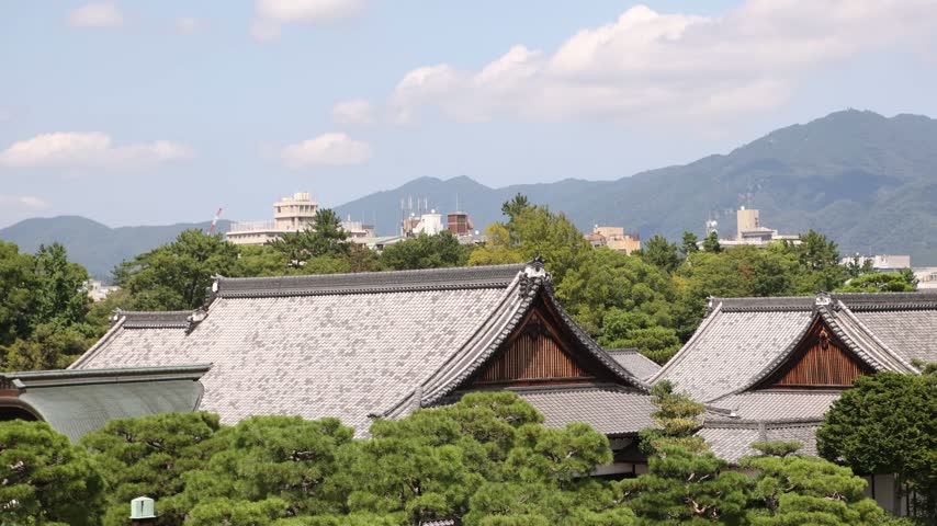 View across the traditional rooftops and historic grounds of Nijo Castle in Kyoto, Japan, with the Ninomaru Palace complex set against distant mountains and the surrounding city