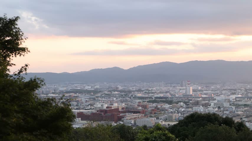 Elevated view over Kyoto from the slopes of Mount Inari near Fushimi Inari Taisha, with the city spreading toward distant hills beneath soft evening light