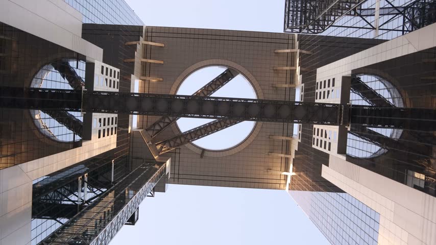 Low-angle view of the distinctive steel structure and geometric architecture of the Umeda Sky Building in Osaka, Japan, with sunlight shining through the modern framework