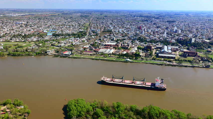 Aerial view of a cargo ship sailing along the Parana River past the Zarate city skyline in Argentina.