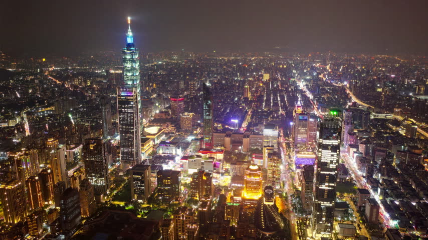 Aerial hyperlapse at night above Downtown Taipei, the vibrant capital city of Taiwan, with  Tower standing out amid modern skyscrapers in XinYi Commercial District and city lights dazzling under twilight sky.