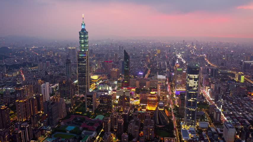 An aerial hyperlapse footage at night above Downtown Taipei, the vibrant capital city of Taiwan, with 101 Tower standing out admid modern skyscrapers in XinYi Commercial District and city lights dazzling under twilight sky.