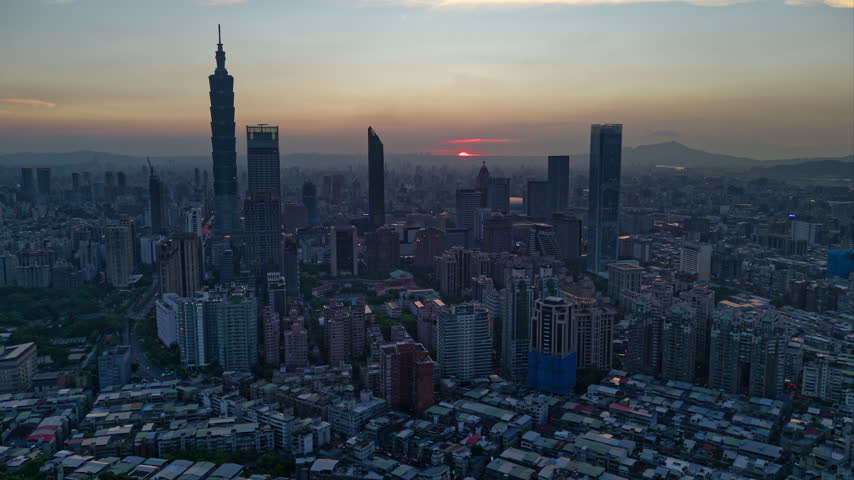 Aerial hyperlapse at night above Downtown Taipei, the vibrant capital city of Taiwan, with  Tower standing out amid modern skyscrapers in XinYi Commercial District and city lights dazzling under twilight sky.