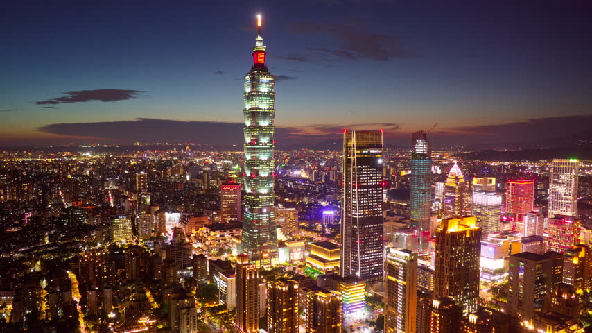 An aerial hyperlapse footage at nightfall above Downtown Taipei, the vibrant capital city of Taiwan, with 101 Tower standing out amid modern skyscrapers in XinYi Commercial District and city lights dazzling under twilight sky.