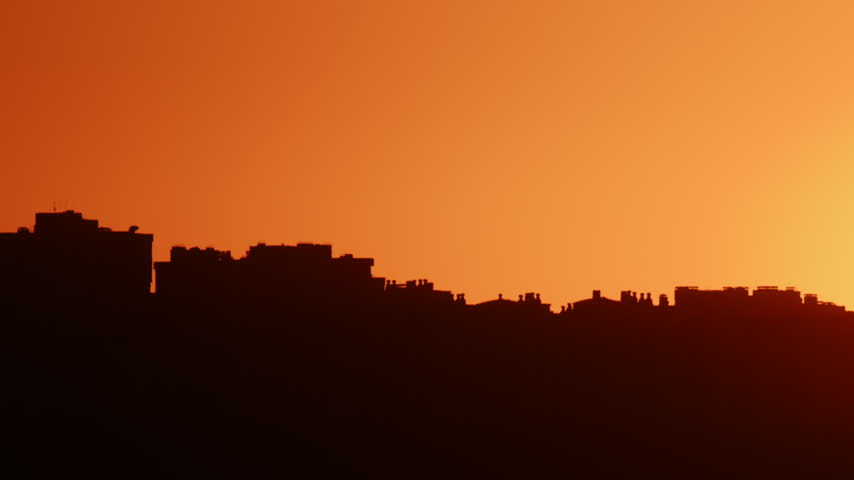 Silhouette of an urban skyline against a vivid orange sunset sky