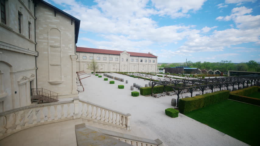 Wide panoramic view of wineryin Moldova, showing the elegant courtyard, historic buildings, terraces, hedges, barrels, and open sky