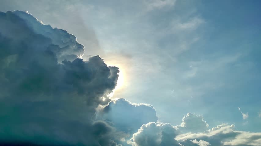 Time lapse of dark storm clouds moving across the sky with bright sun shining behind and god rays beaming through, dramatic weather transition