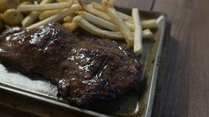 Juicy grilled t-bone steak served on a platter with two whole salted potatoes on a wooden table