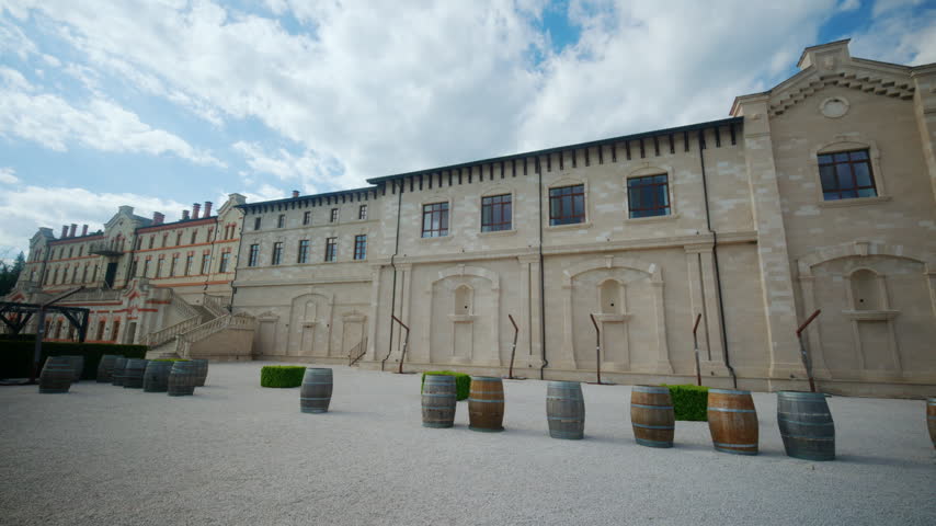 Wide courtyard view at winery castle in Moldova, showing historic winery buildings, stone facades, wine barrels, gravel pathways, and architectural staircases