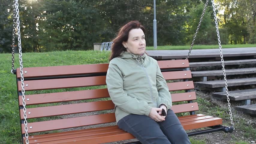 Pensive Woman Swinging on Swing in City Park.