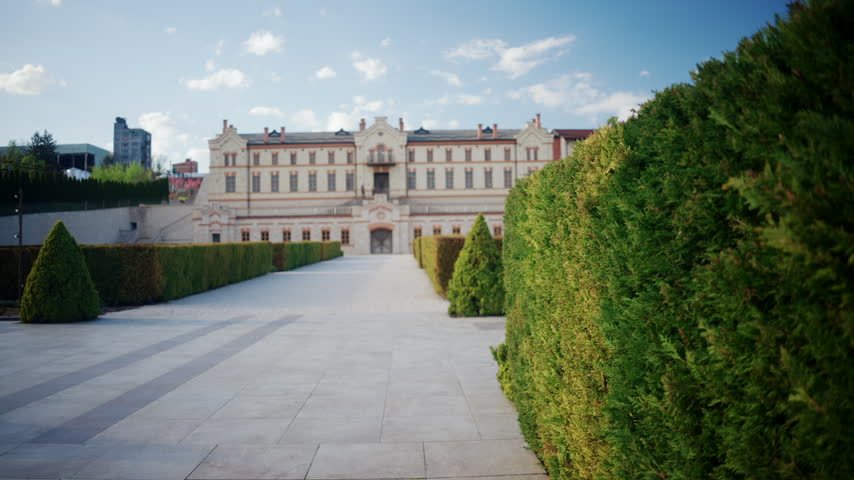 Wide scenic view of the large open courtyard at winery castle in Moldova, featuring historic winery buildings, decorative string lights, wine barrels, trimmed hedges, and a bright blue sky