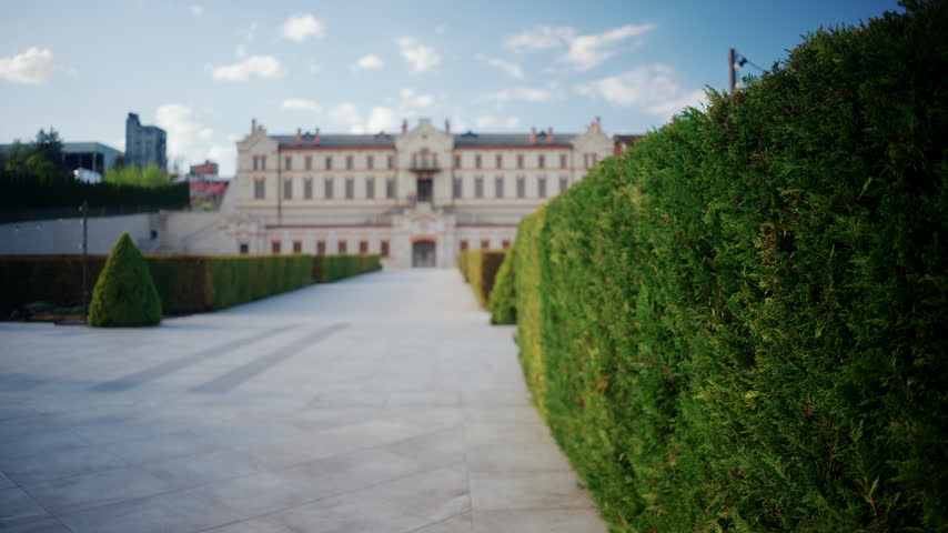Wide scenic view of the large open courtyard at winery castle in Moldova, featuring historic winery buildings, decorative string lights, wine barrels, trimmed hedges, and a bright blue sky