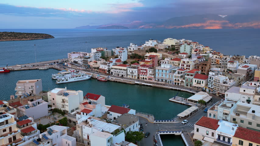 Aerial drone view of the harbor town on its rocky peninsula with colorful waterfront buildings, Agios Nikolaos, Greece