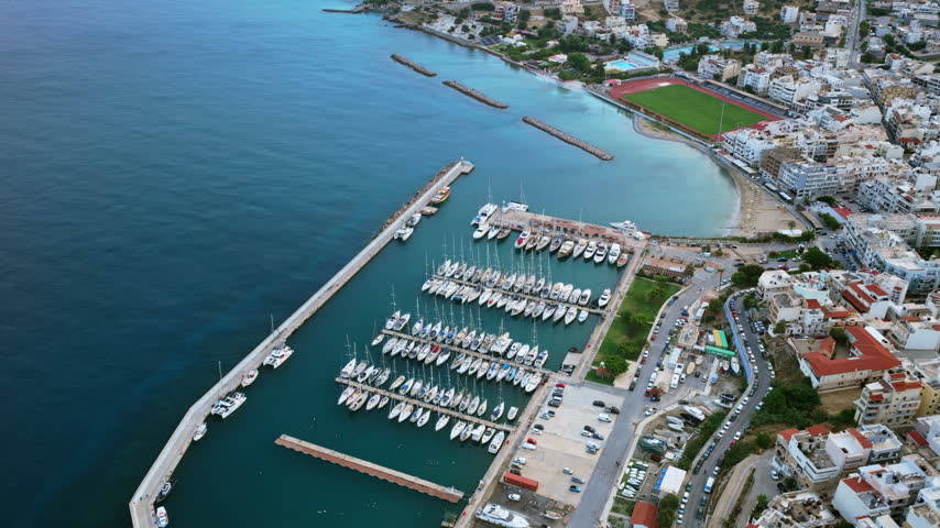 Aerial drone view of the marina filled with moored yachts and sailboats beside the town, Agios Nikolaos, Greece