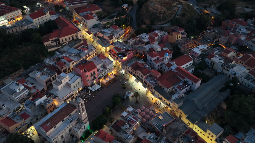 Aerial drone view of a lively old town street lined with tavernas and a domed church, Chania, Greece