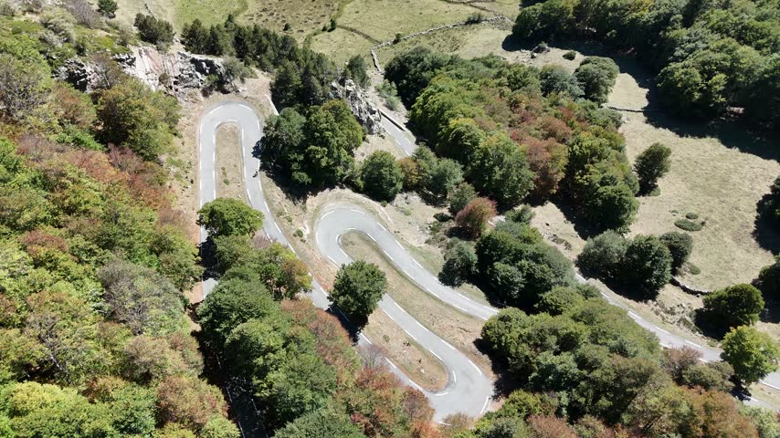Aerial view of two cyclists riding up the hairpin turns of a winding mountain road in the Pyrenees