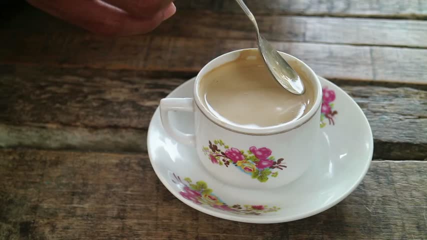 A spoon stirs a frothy cappuccino in a classic cup.