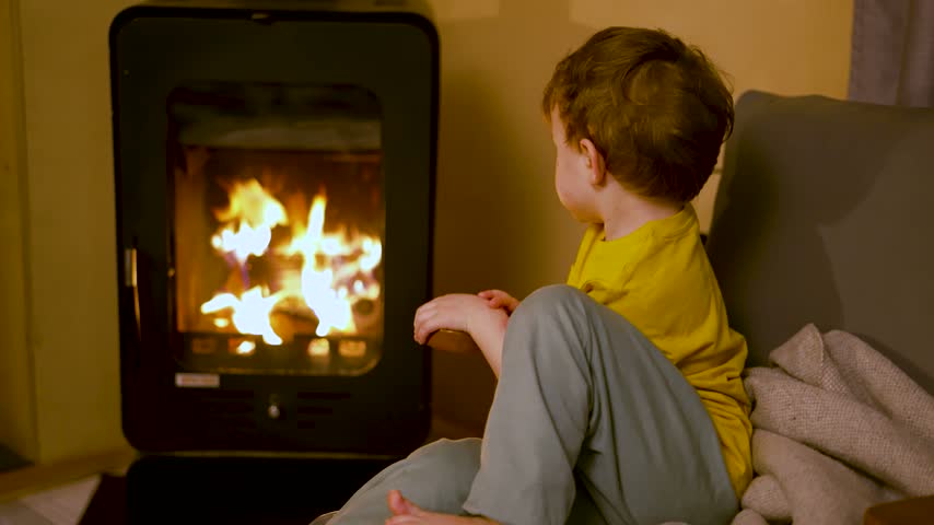 Curious toddler captivated by dancing flames while observing fire in warm living room. Young learner focused on studying warmth and light from fireplace.