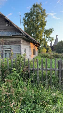 Old wooden house near a fence with green grass and trees in the background