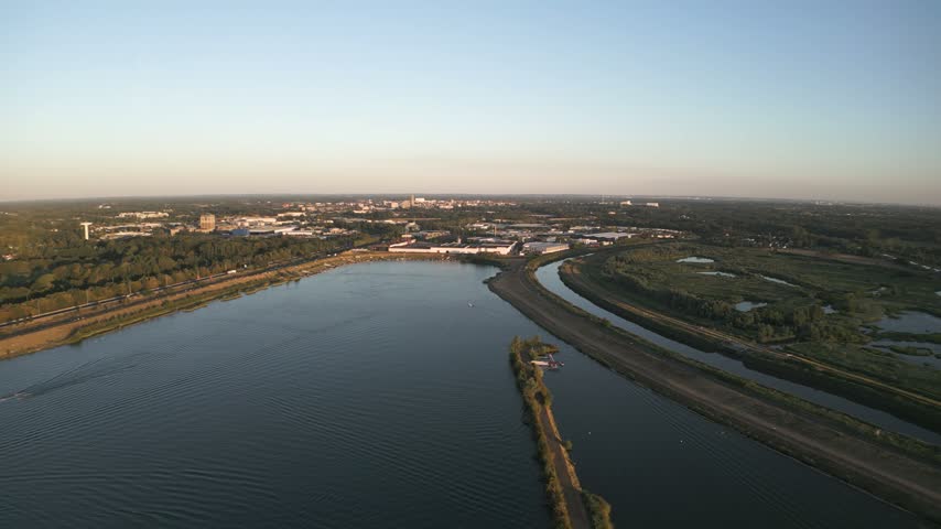 Scenic aerial shot of the river and dam in Mechelen, Belgium, featuring a boat on calm water and surrounding landscape.